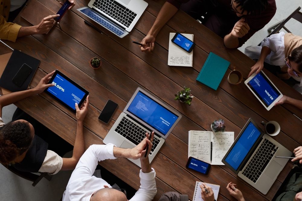 Corporate meeting birds eye view with people sitting around a table on their devices