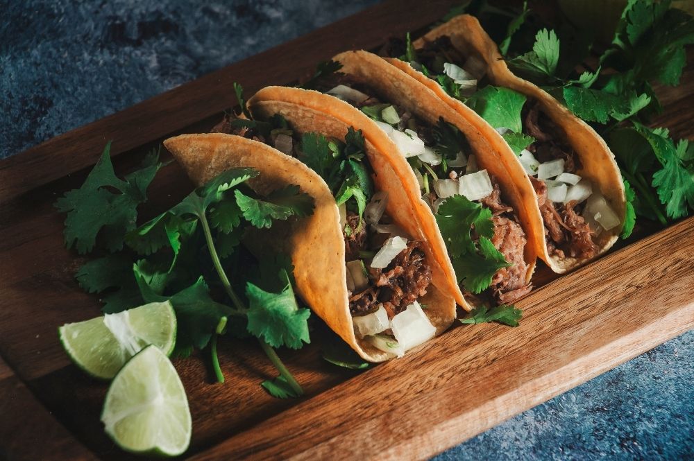 3 tacos on a wooden board with garnishes